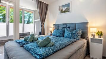 Een slaapkamer met een groot bed, een hoofdbord, nachtkastje, lamp en een raam met gordijnen.