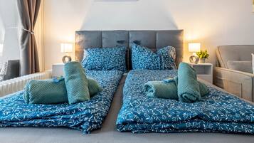 A double bed with matching blue floral bedding, two bedside tables with lamps, a grey sofa, and a wall-mounted picture.