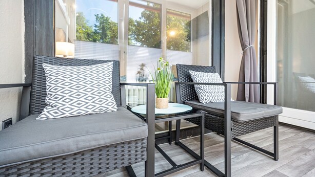 Un balcon agrémenté de meubles en osier, d’une table en verre et d’une plante en pot.