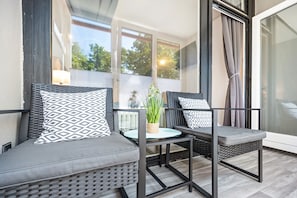 Un balcon agrémenté de meubles en osier, d’une table en verre et d’une plante en pot.