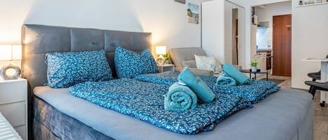 A neatly arranged bedroom with a large bed, bedside tables, a lamp, and a view into the adjacent room.
