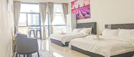 A hotel room with two beds, a dining area, and a large window with curtains.