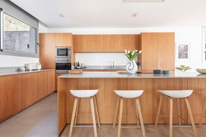 Eine moderne Küche mit Holzschränken, einer zentralen Kochinsel mit Barhocker, einer Mikrowelle, einem Backofen und einer Vase mit Blumen.