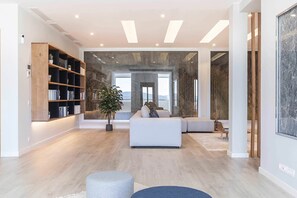 Ein modernes Wohnzimmer mit einer Couch, einem Bücherregal, einer Topfpflanze und einem großen Fenster.