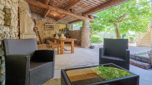 Ein Außenbereich mit einer Terrasse, Korbmöbeln, einer Steinwand und einer Holzbalkendecke.