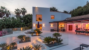 A modern house with a glass-enclosed patio, outdoor furniture, and a dining area. - Villa Isola Bianca with pool - My Rental Homes (Playa De Talamanca)