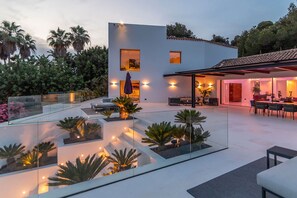 A modern house with a glass-enclosed patio, outdoor furniture, and a dining area. - Villa Isola Bianca with pool - My Rental Homes (Playa De Talamanca)