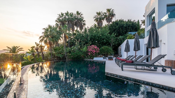 A modern infinity pool with lounge chairs and umbrellas, surrounded by lush greenery and palm trees. - Villa Isola Bianca with pool - My Rental Homes (Playa De Talamanca)