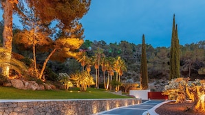 A landscaped pathway with a stone wall, palm trees, and a tall coniferous tree. - Villa Isola Bianca with pool - My Rental Homes (Playa De Talamanca)