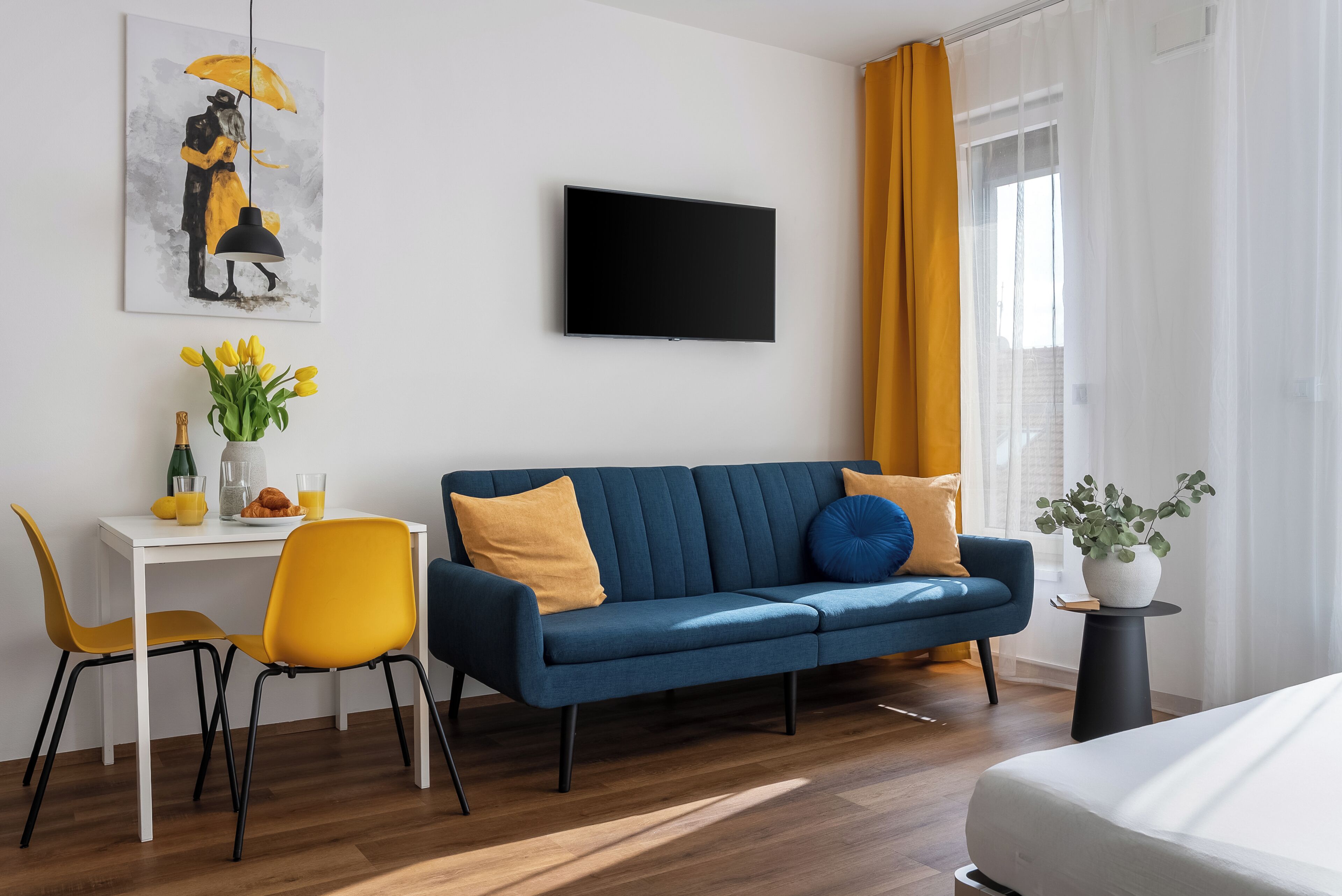 Et moderne værelse med en blå sofa, et hvidt skrivebord, gule stole og et fladskærms-tv.