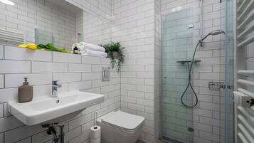 A modern bathroom with white tiles, a glass shower enclosure, a sink, and a toilet.