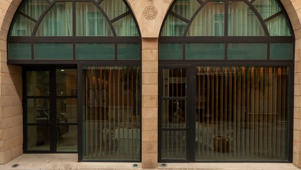 A building facade with large arched windows, a central decorative element, and a door with vertical bars. - Souvirón de Torres III (Málaga)