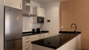 A modern kitchen with a stainless steel refrigerator, white cabinetry, a black countertop, and a built-in oven. - Souvirón de Torres III (Málaga)