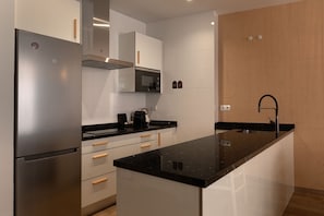 Eine moderne Küche mit Edelstahl-Kühlschrank, weißen Schränken, einer schwarzen Arbeitsplatte und einem eingebauten Backofen.