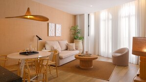 A modern living room with a sofa, a dining table, chairs, a coffee table, a floor lamp, a hanging light fixture, a potted plant, and a large window with curtains. - Souvirón de Torres III (Málaga)