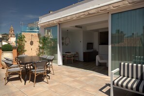 Eine Terrasse mit Tisch, Stühlen und einer Couch, sowie eine Glastür, die zu einem Innenbereich führt.
