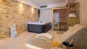 Ein Spa-Raum mit Steinwand, Whirlpool, einer in Glas abgeschirmten Dusche und einer Holzablage mit Handtüchern.