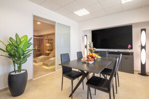 Et moderne spiseområde med et stort bord, sorte stole, en potteplante og et fladskærms-TV.