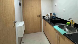 Une cuisine de taille réduite avec une porte en bois, un plan de travail noir, un évier et un sol carrelé.