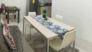 Un espace de vie compact comprenant une table à manger, un canapé avec des coussins à motifs léopard, un petit coin cuisine et un ventilateur.