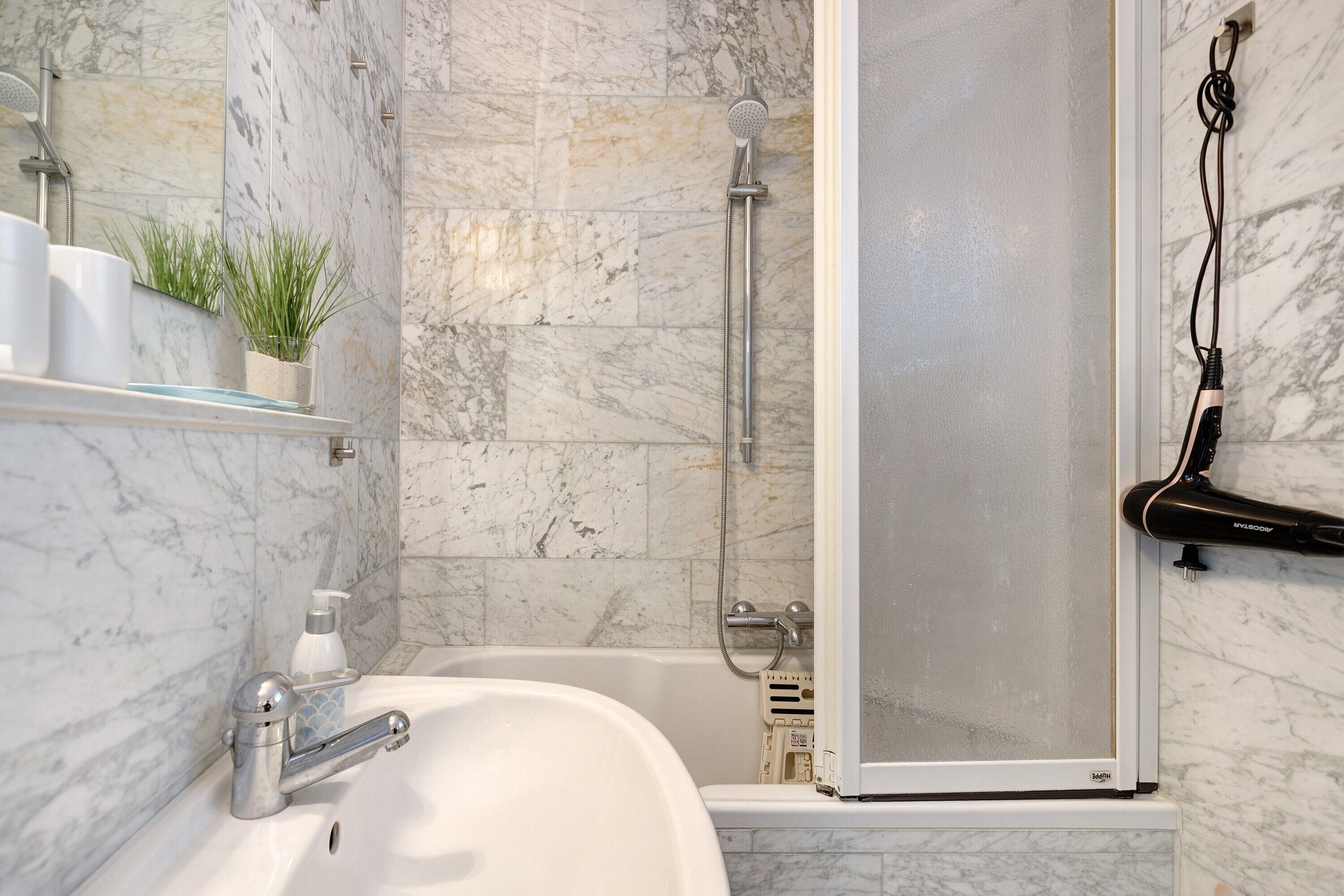 A bathroom with a marble wall, a bathtub, a shower, a glass-enclosed shower, and a towel rack.