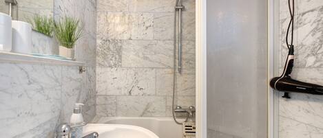 A bathroom with a marble wall, a bathtub, a shower, a glass-enclosed shower, and a towel rack.