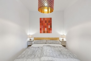 Ein Schlafzimmer mit einem Bett, zwei Nachttischen, einer Lampe, einer gemusterten Tagesdecke, einem Wandbild und einer Hängelampe.