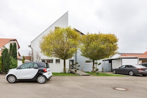 Eine Wohnstraße mit einem weißen Auto, das vor einem Haus mit geneigtem Dach und Garage geparkt ist.