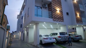 A multi-story residential building with a covered parking area and a narrow street leading to the entrance. - L Rina Apartment (Lekki)