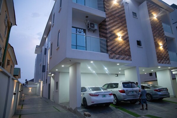 A multi-story residential building with a covered parking area and a narrow street leading to the entrance. - L Rina Apartment (Lekki)
