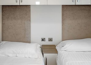 Ein Hotelzimmer mit zwei Betten, einem Holzkopfstück und einer weißen Wand mit zwei Steckdosen.