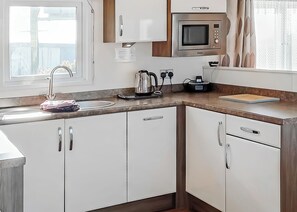 A modern kitchen with a sink, microwave, kettle, and a window with curtains. - 2 bedroom accommodation in Looe (Looe)