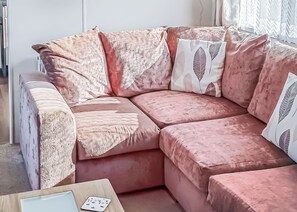 A pink sectional sofa with fringed throw pillows and a card game on the side. - 2 bedroom accommodation in Looe (Looe)