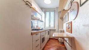 A narrow kitchen with white cabinets, a stove, and a window with curtains. - D&R Apartment - Metro Re di Roma (Rome)
