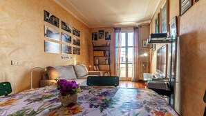 A living room with a sofa, a coffee table with a floral tablecloth, a bookshelf, and a laptop on a glass table. - D&R Apartment - Metro Re di Roma (Rome)