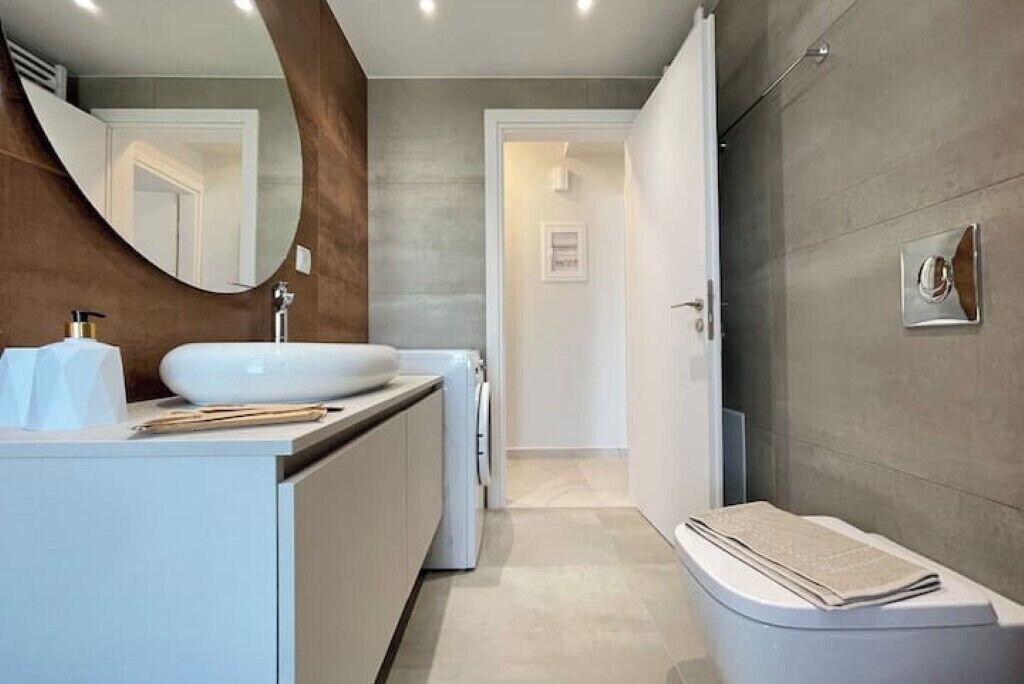 Ein modernes Badezimmer mit großem Spiegel, Waschbecken in Weiß und Toilette.