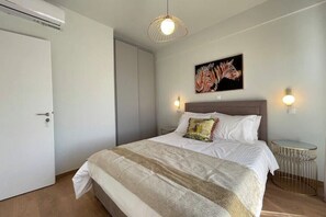 Une chambre à coucher avec un lit, un tableau, une lampe fixée au mur et une petite table ronde.