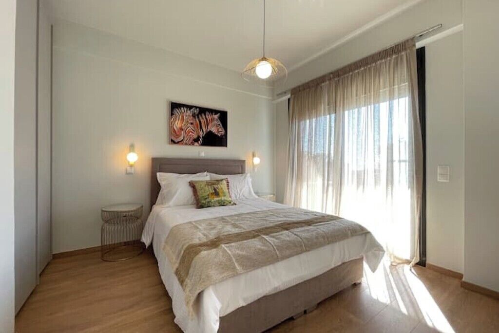 A bedroom with a bed, a round side table, a wall-mounted zebra painting, and a large window with curtains.