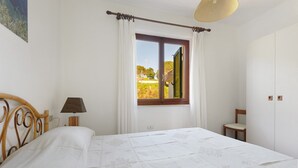 Une chambre à coucher avec un lit, une fenêtre avec des rideaux, une chaise et une lampe.
