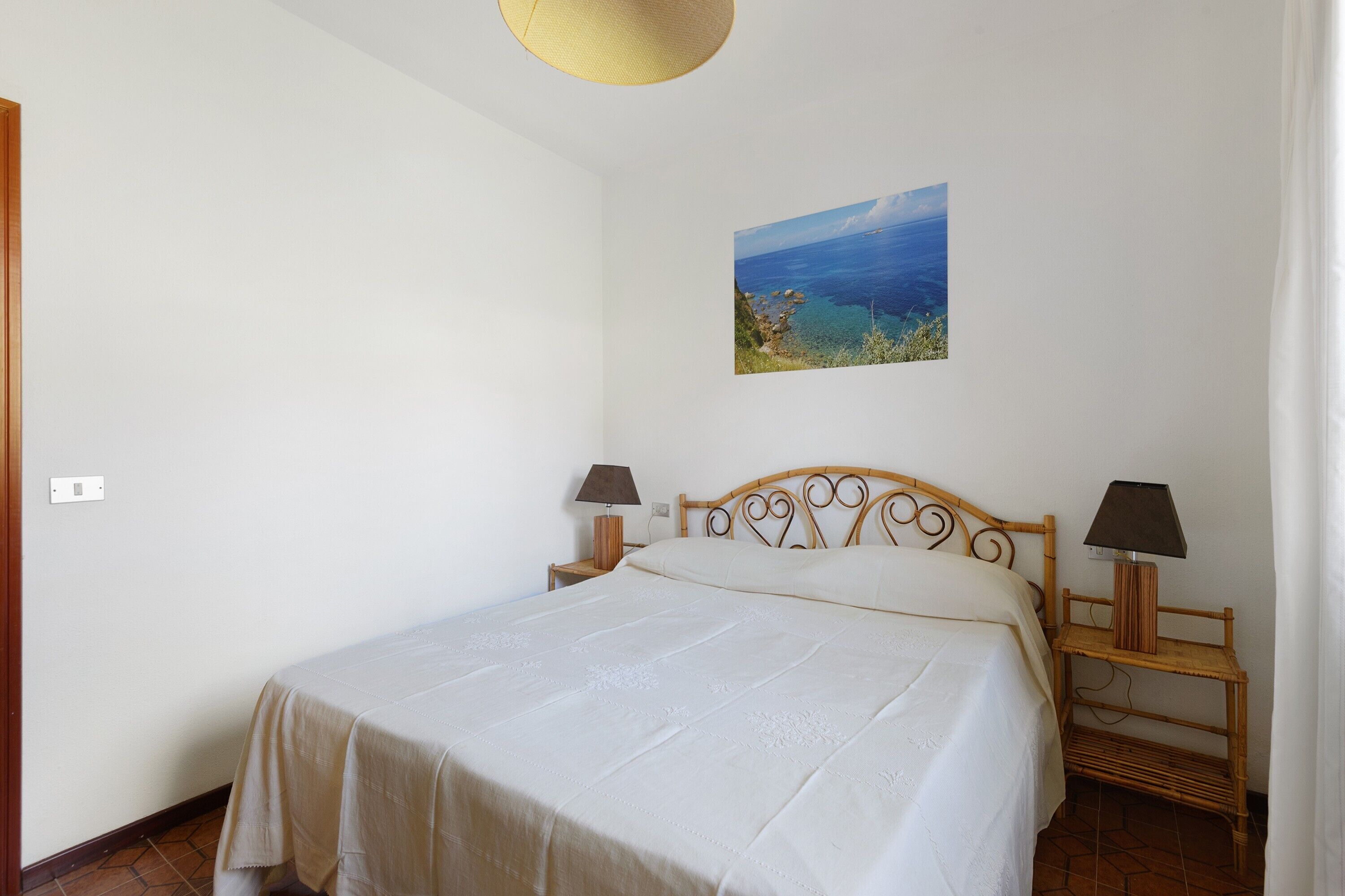 Camera da letto con un letto, due comodini con lampade, un quadro appeso al muro e una lampada a soffitto con decorazioni.