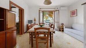 Un coin repas avec une table en bois, des chaises, un luminaire suspendu et une vue dégagée sur l’extérieur grâce à une grande fenêtre.