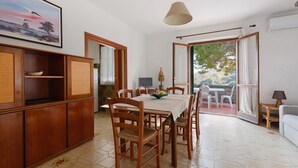 Un espace repas comprenant une table, des chaises et une vue sur l’extérieur grâce à une porte ouverte.