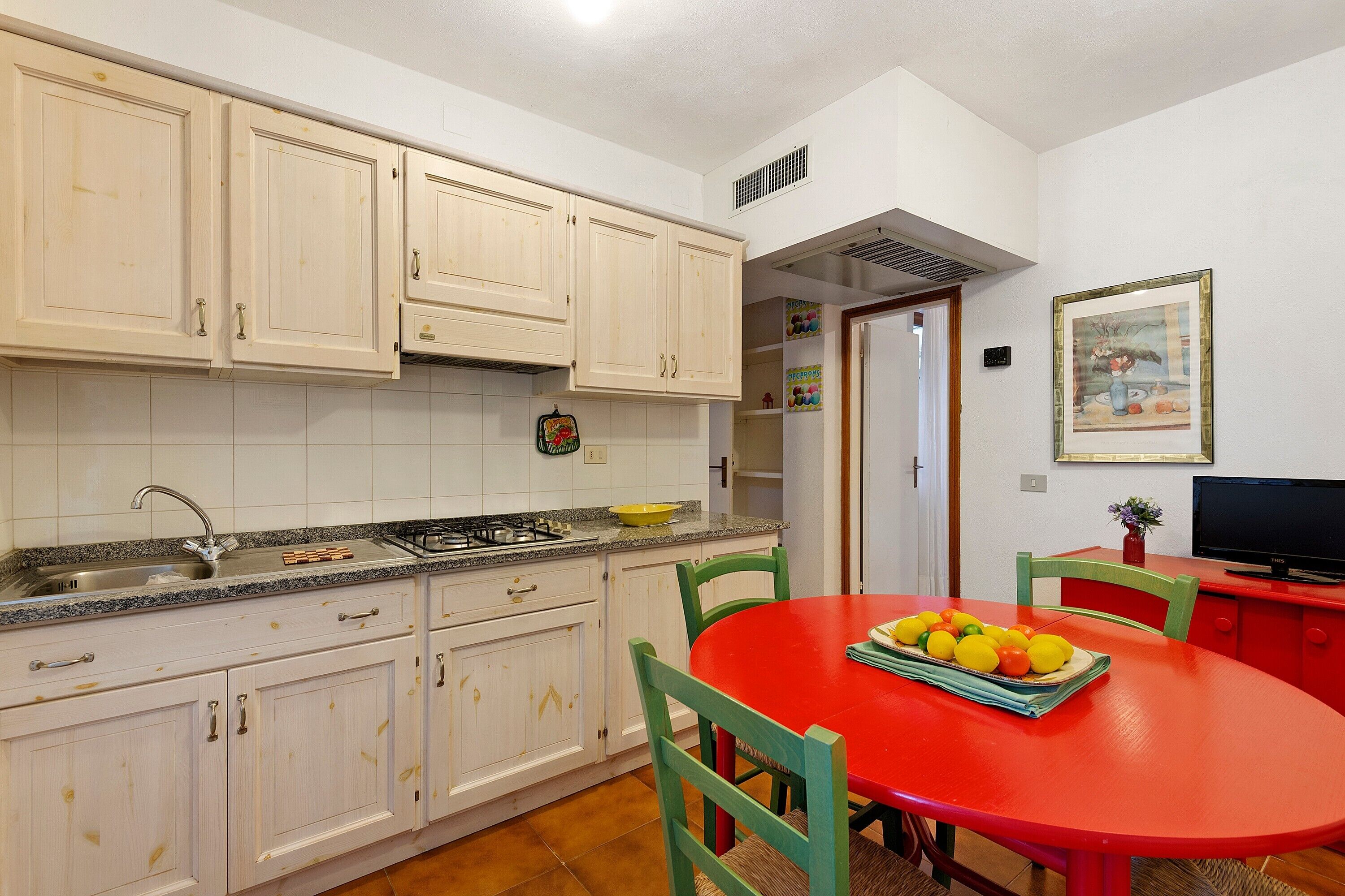 A kitchen with white cabinets, a red dining table, and a television.