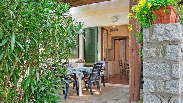 Une terrasse extérieure avec une table et des chaises, entourée de verdure et d’un mur en pierre.
