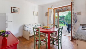 Un coin repas avec une table et des chaises rouges, un canapé et un espace cuisine avec une fenêtre.