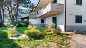 Un bâtiment à deux étages doté d’un balcon, entouré de verdure et d’arbres.