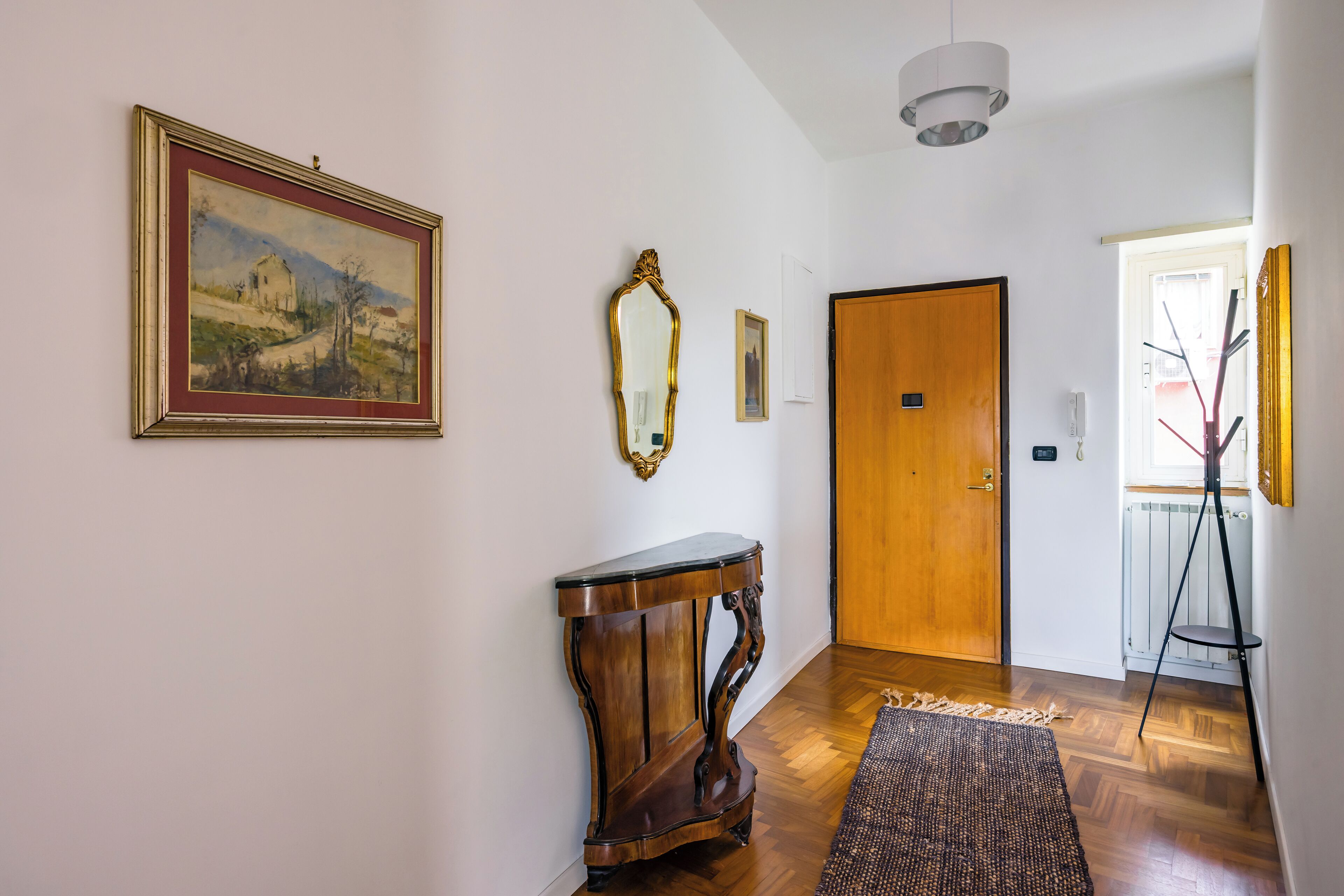 A hallway with a wooden door, a framed painting, a mirror, and a small table.
