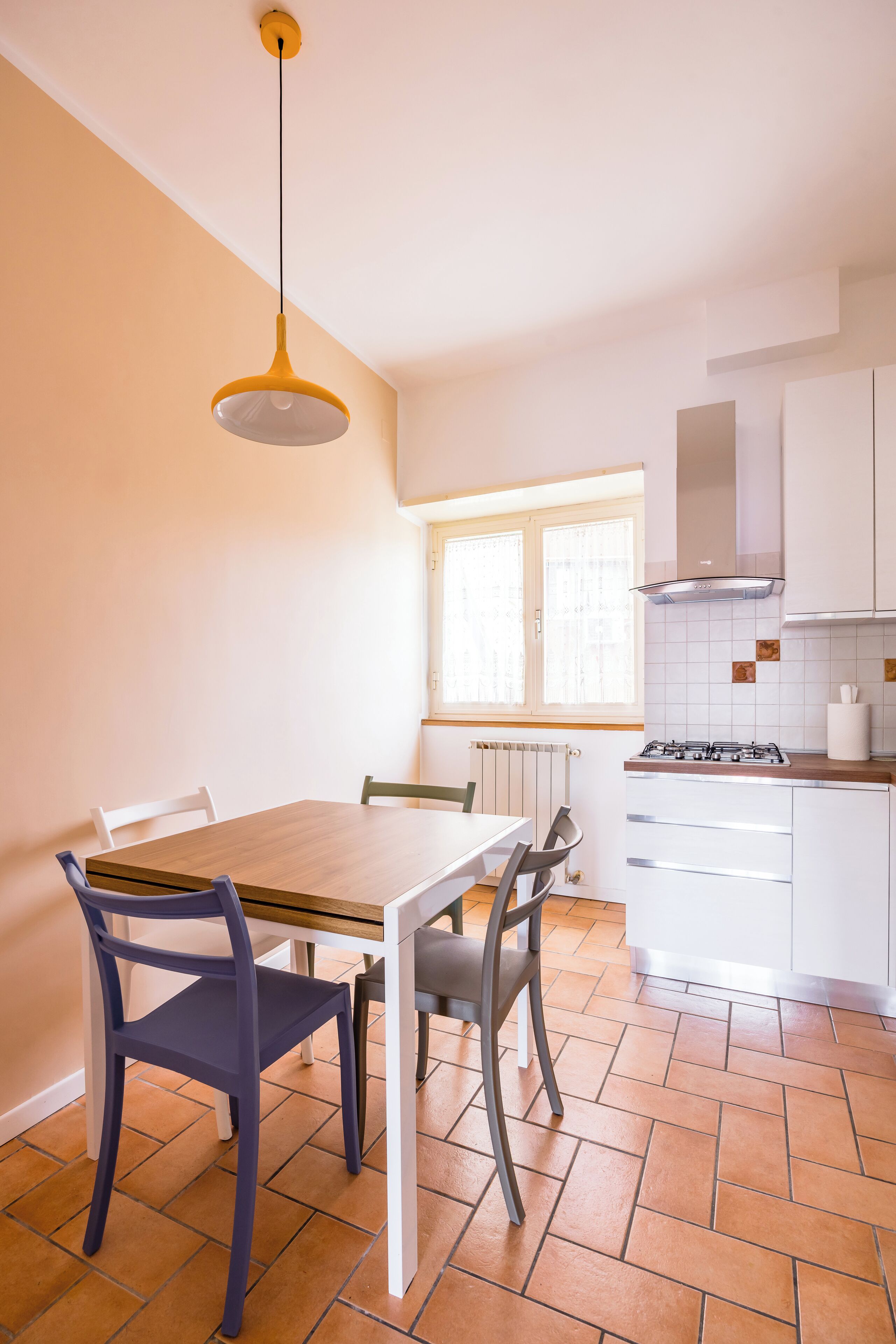 A kitchen with a dining table, chairs, a hanging light fixture, and a window.