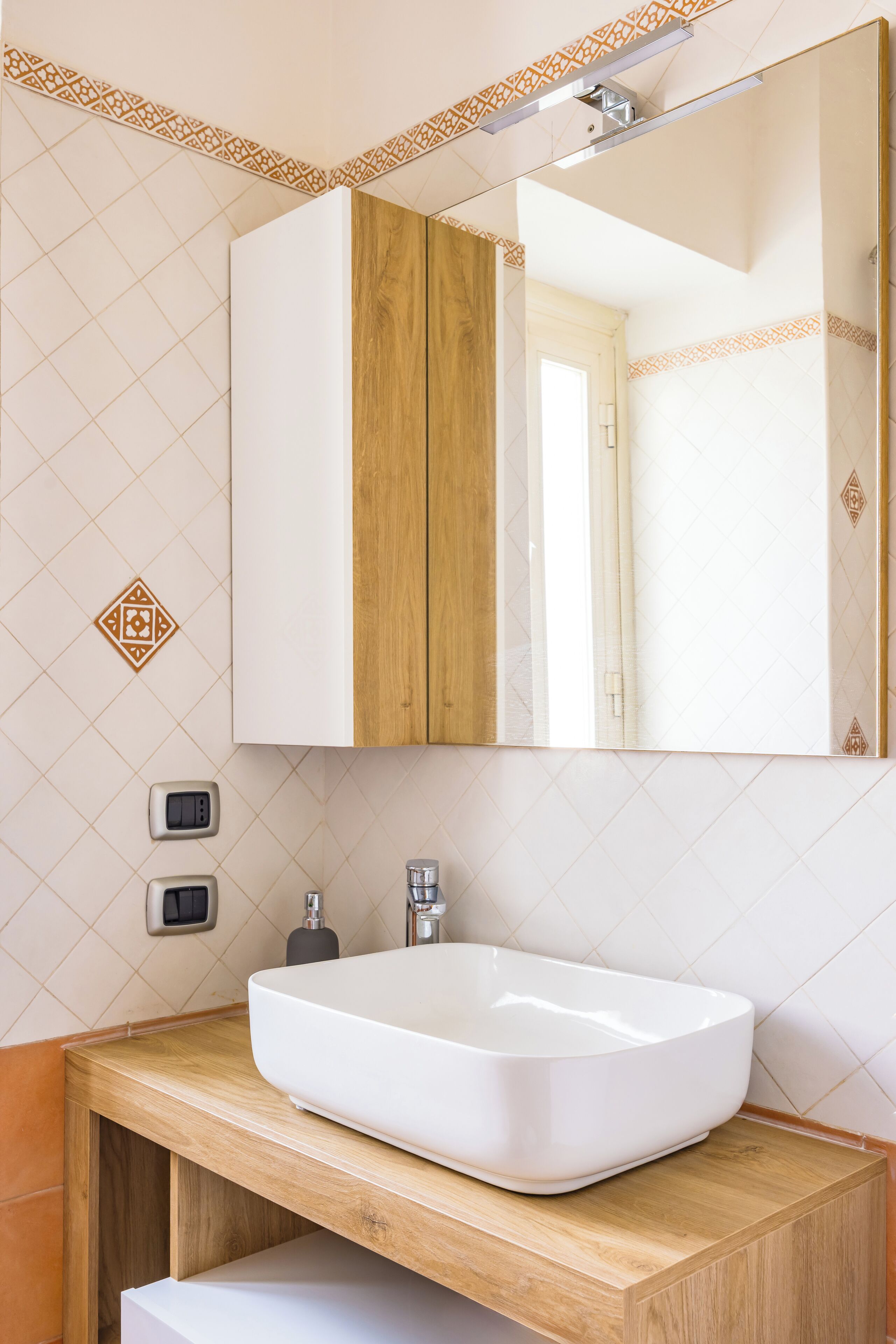 Un bagno con lavandino bianco, mobile contenitore in legno e specchio.