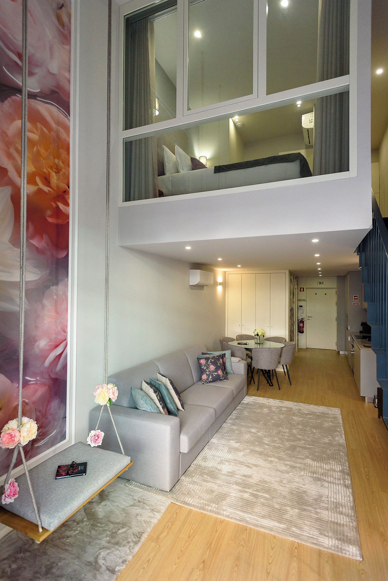 A modern interior with a grey sofa, a dining table, and a staircase leading to an upper level.